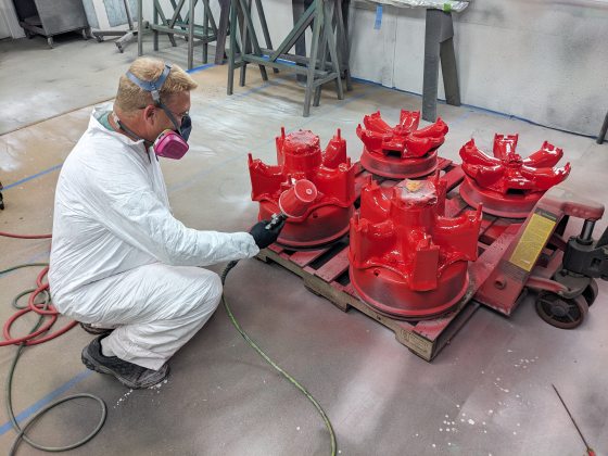 A person in a white tyvec suit and mask spray painting truck wheels.